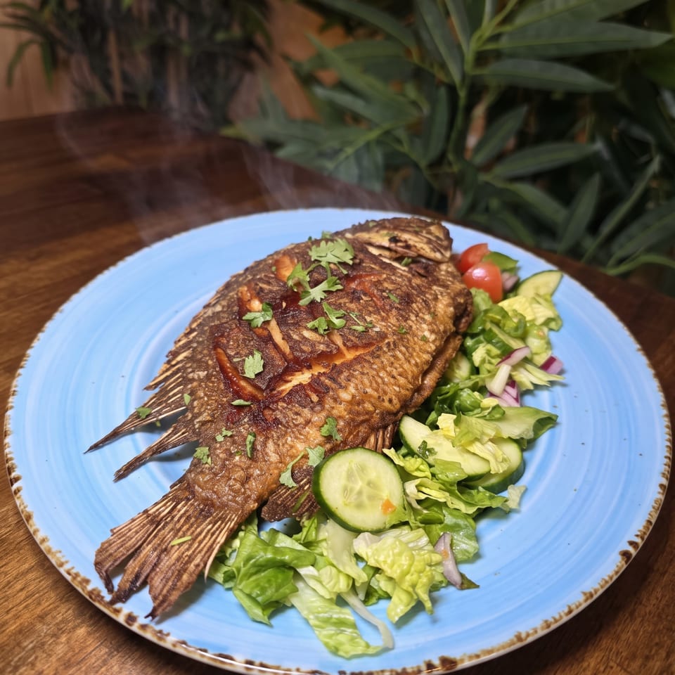 Whole fried fish garnished with cilantro and sauce, served with cucumber salad on a blue plate at a wooden table.
